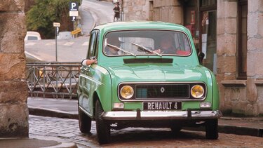 Grüner Renault R4 fährt mit zwei Insassen durch die Gassen