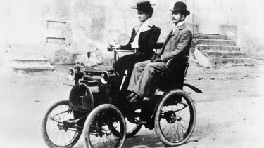 Der junge Louis Renault fährt einen mit einem Renault Prototyp durch die Straßen von Paris 1898